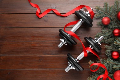 Photo of Dumbbells, fir tree branches and Christmas baubles on wooden table, flat lay. Space for text