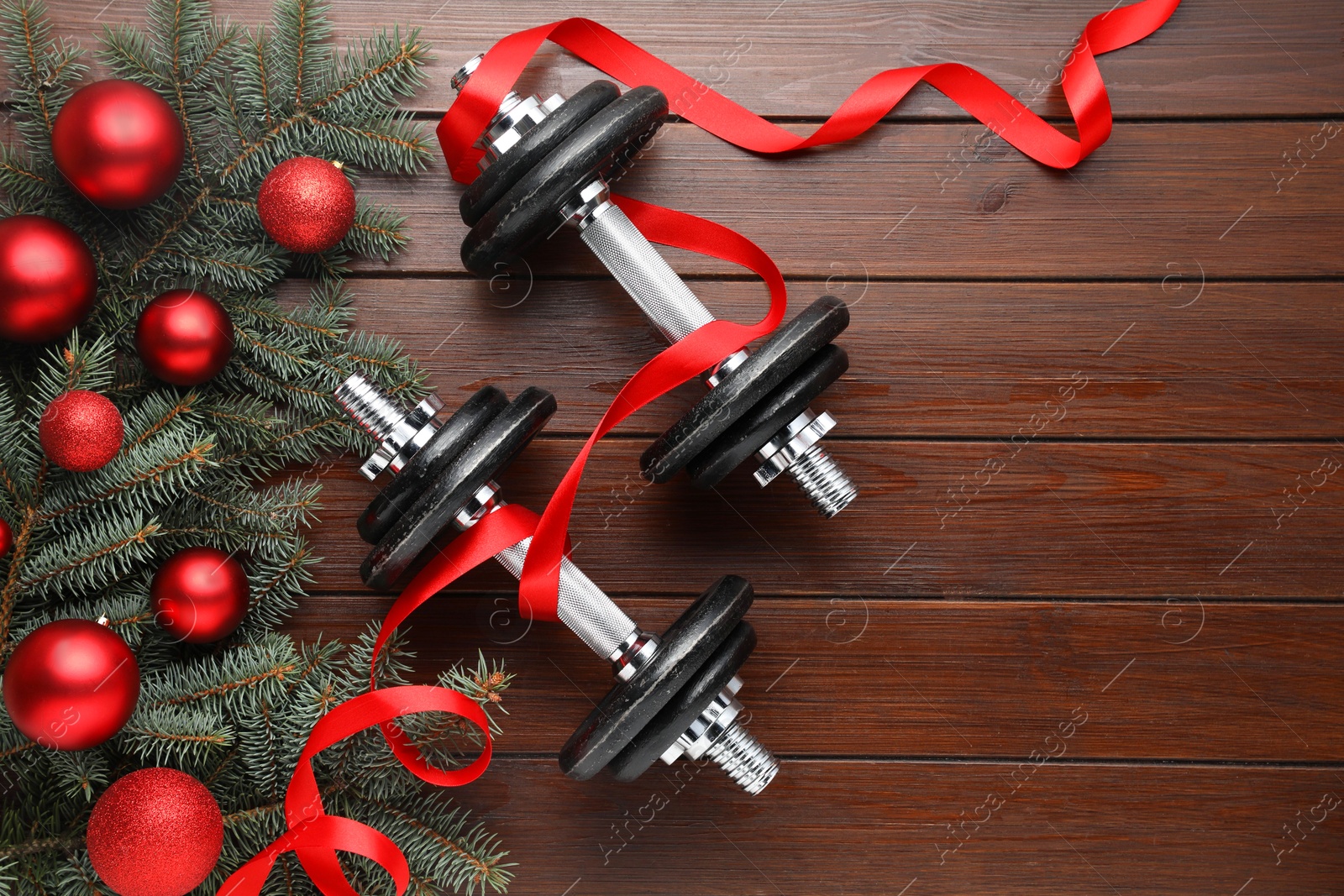 Photo of Dumbbells, fir tree branches and Christmas baubles on wooden table, flat lay. Space for text