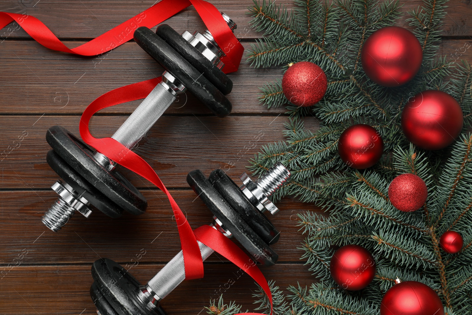 Photo of Dumbbells, fir tree branches and Christmas baubles on wooden table, flat lay. Space for text