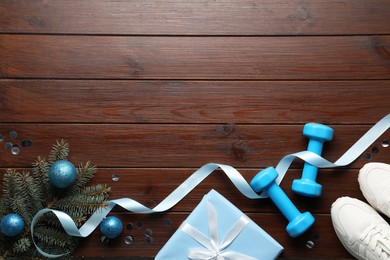 Photo of Dumbbells, sneakers, fir tree branches and Christmas decor on wooden table, flat lay. Space for text