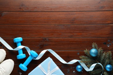 Photo of Dumbbells, sneakers, fir tree branches and Christmas decor on wooden table, flat lay. Space for text