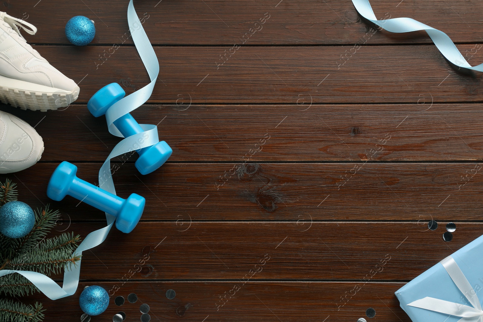 Photo of Dumbbells, sneakers, fir tree branches and Christmas decor on wooden table, flat lay. Space for text