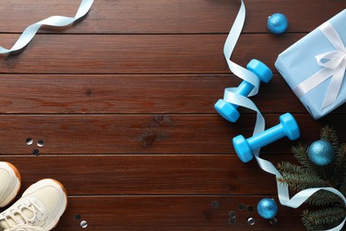 Photo of Dumbbells, sneakers, fir tree branches and Christmas decor on wooden table, flat lay. Space for text