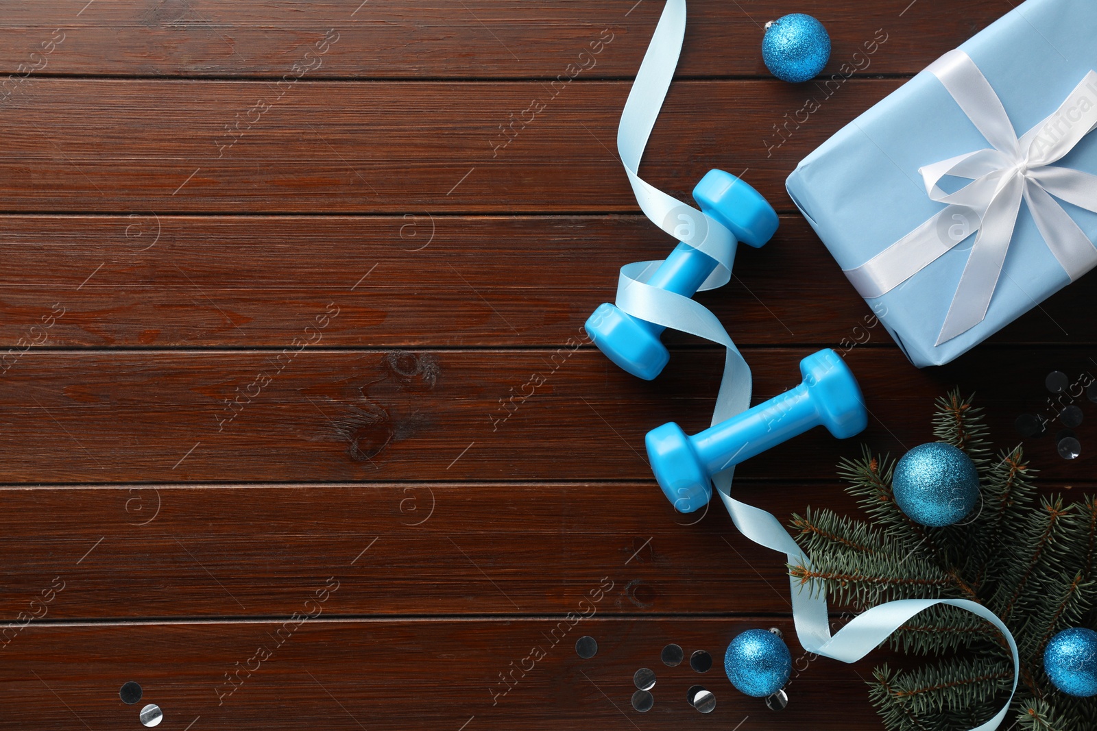 Photo of Dumbbells, fir tree branches and Christmas decor on wooden table, flat lay. Space for text