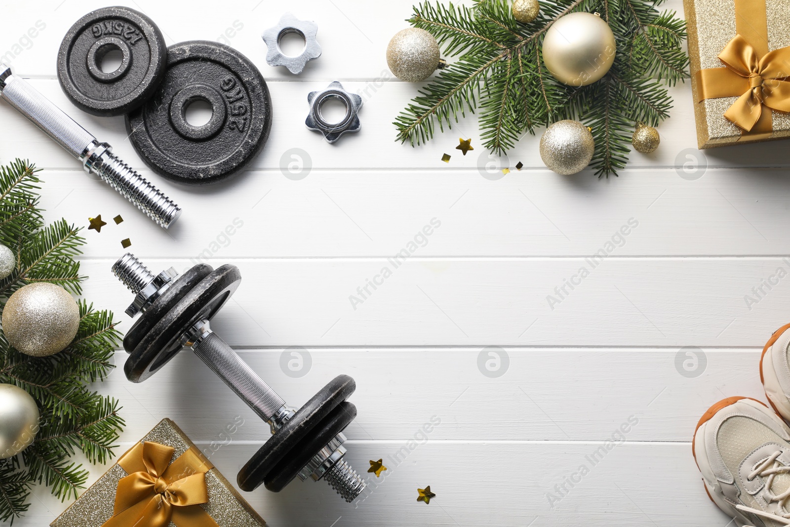 Photo of Dumbbells, fir tree branches, sneakers and Christmas baubles on white wooden table, flat lay. Space for text