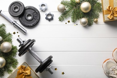 Dumbbells, fir tree branches, sneakers and Christmas baubles on white wooden table, flat lay. Space for text