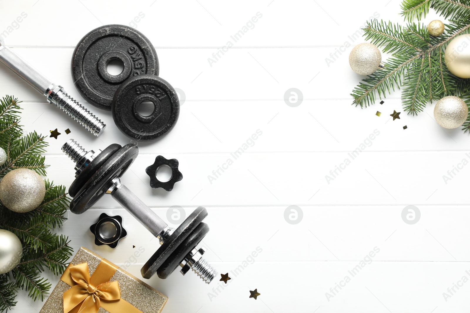 Photo of Dumbbells, fir tree branches and Christmas baubles on white wooden table, flat lay. Space for text