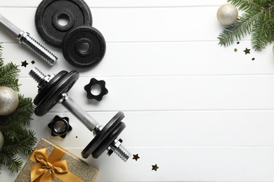 Photo of Dumbbells, fir tree branches and Christmas baubles on white wooden table, flat lay. Space for text