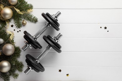 Photo of Dumbbells, fir tree branches and Christmas baubles on white wooden table, flat lay. Space for text