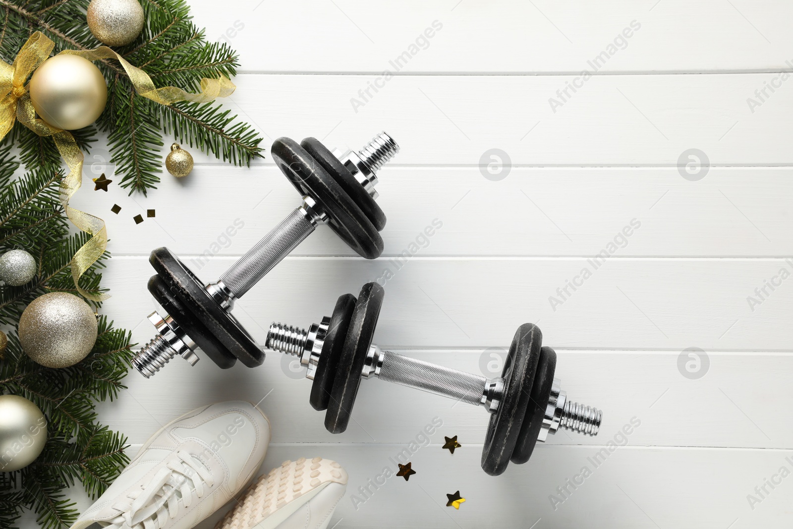 Photo of Dumbbells, fir tree branches, sneakers and Christmas baubles on white wooden table, flat lay. Space for text