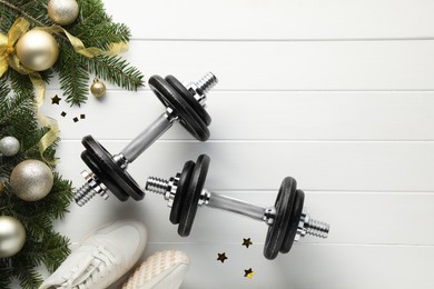 Photo of Dumbbells, fir tree branches, sneakers and Christmas baubles on white wooden table, flat lay. Space for text