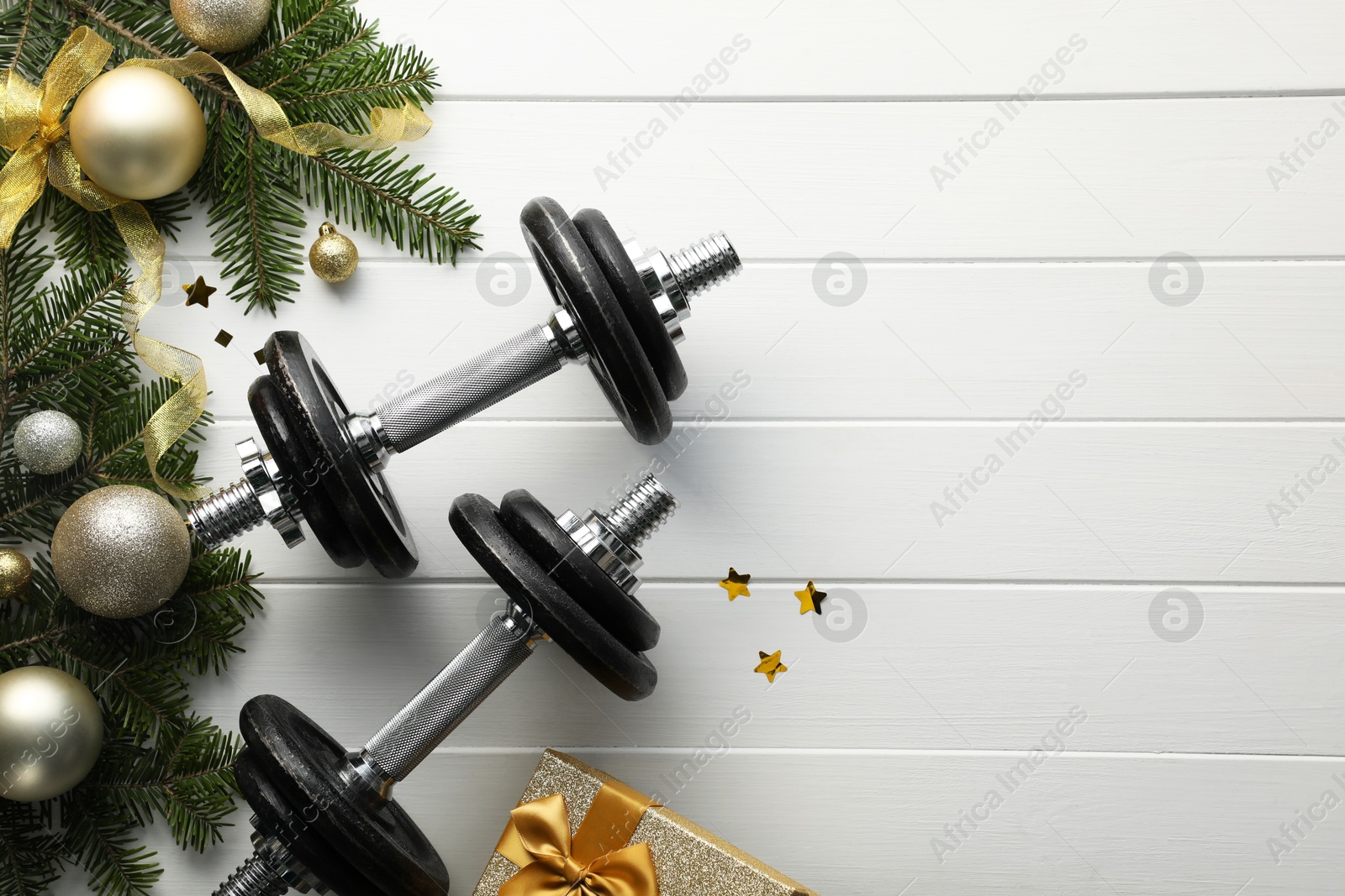 Photo of Dumbbells, fir tree branches and Christmas baubles on white wooden table, flat lay. Space for text