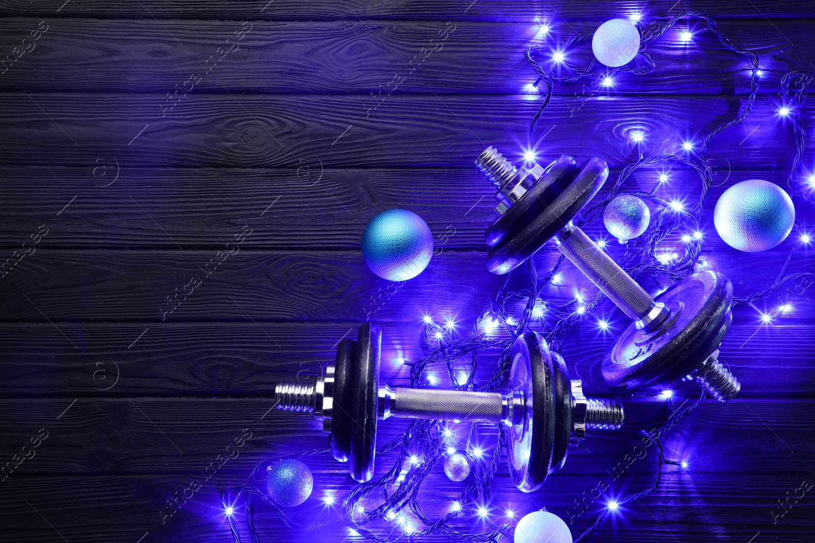 Photo of Dumbbells, baubles and Christmas lights on wooden table, flat lay. Space for text