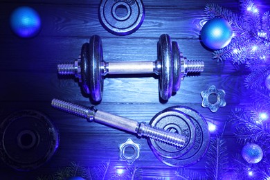 Photo of Dumbbells, fir tree branches, baubles and Christmas lights on wooden table, flat lay