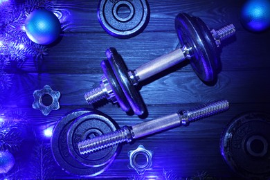 Photo of Dumbbells, fir tree branches, baubles and Christmas lights on wooden table, flat lay