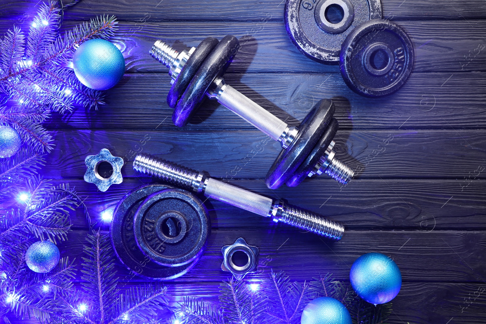 Photo of Dumbbells, fir tree branches, baubles and Christmas lights on wooden table, flat lay