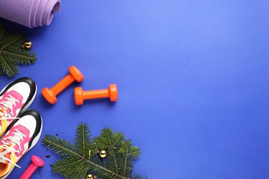 Photo of Christmas baubles, fir tree branches and gym equipment on blue background, flat lay. Space for text