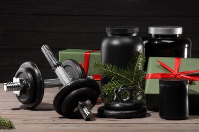 Photo of Dumbbells, containers with supplement and Christmas decor on wooden table