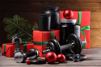 Photo of Dumbbells, containers with supplement and Christmas decor on wooden table