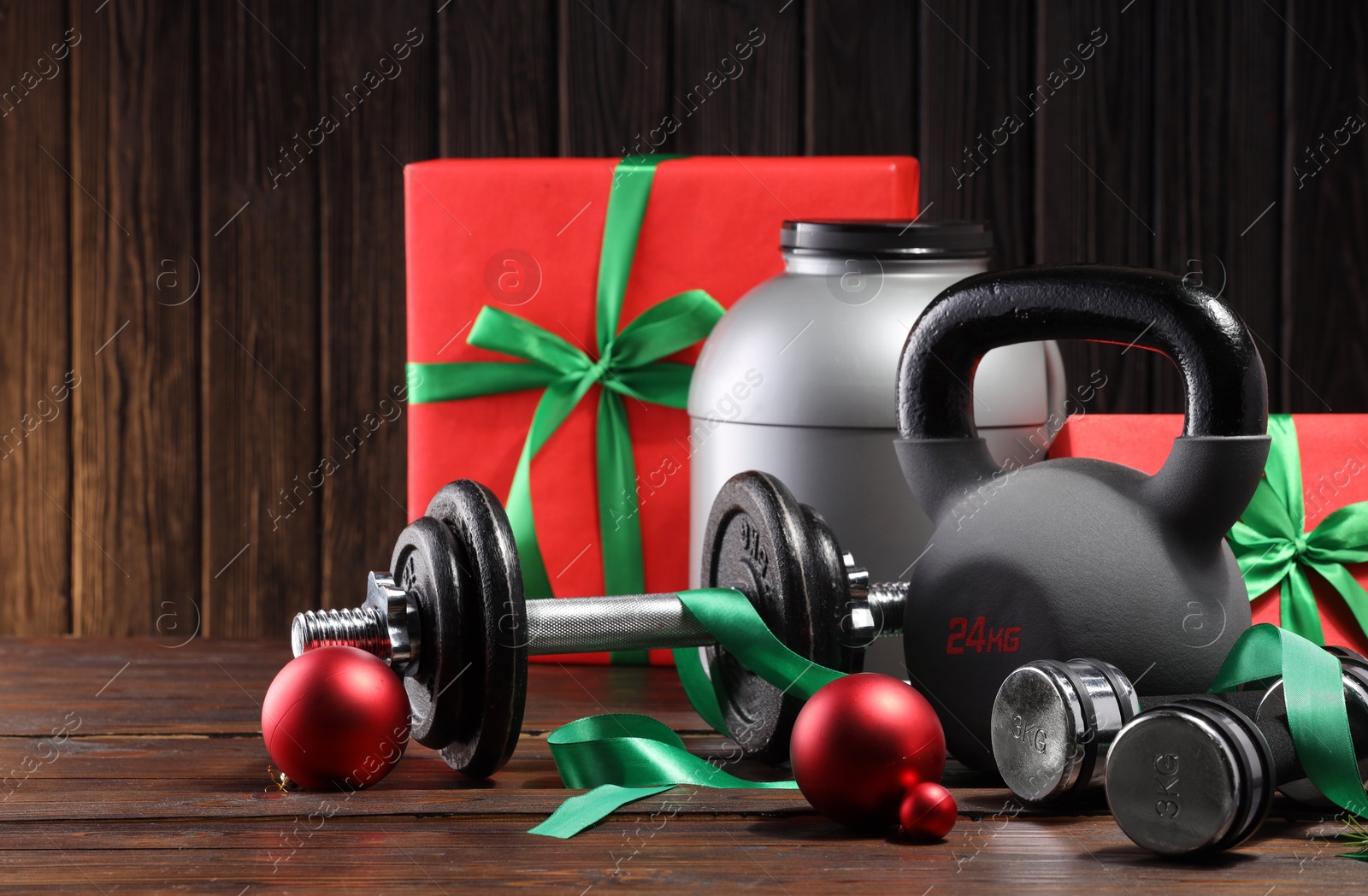 Photo of Dumbbells, container with supplement, kettlebell and Christmas decor on wooden table