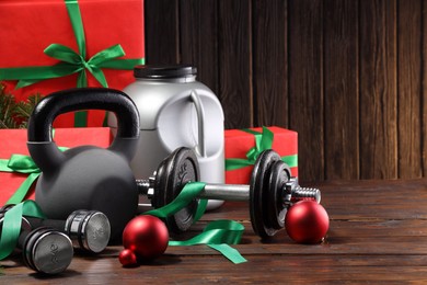 Photo of Dumbbells, container with supplement, kettlebell and Christmas decor on wooden table