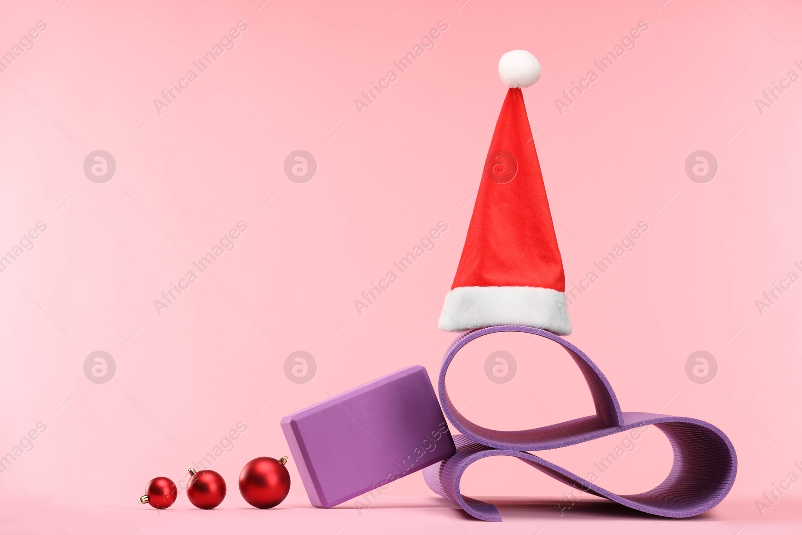 Photo of Yoga mat, Santa hat and baubles on pink background, space for text