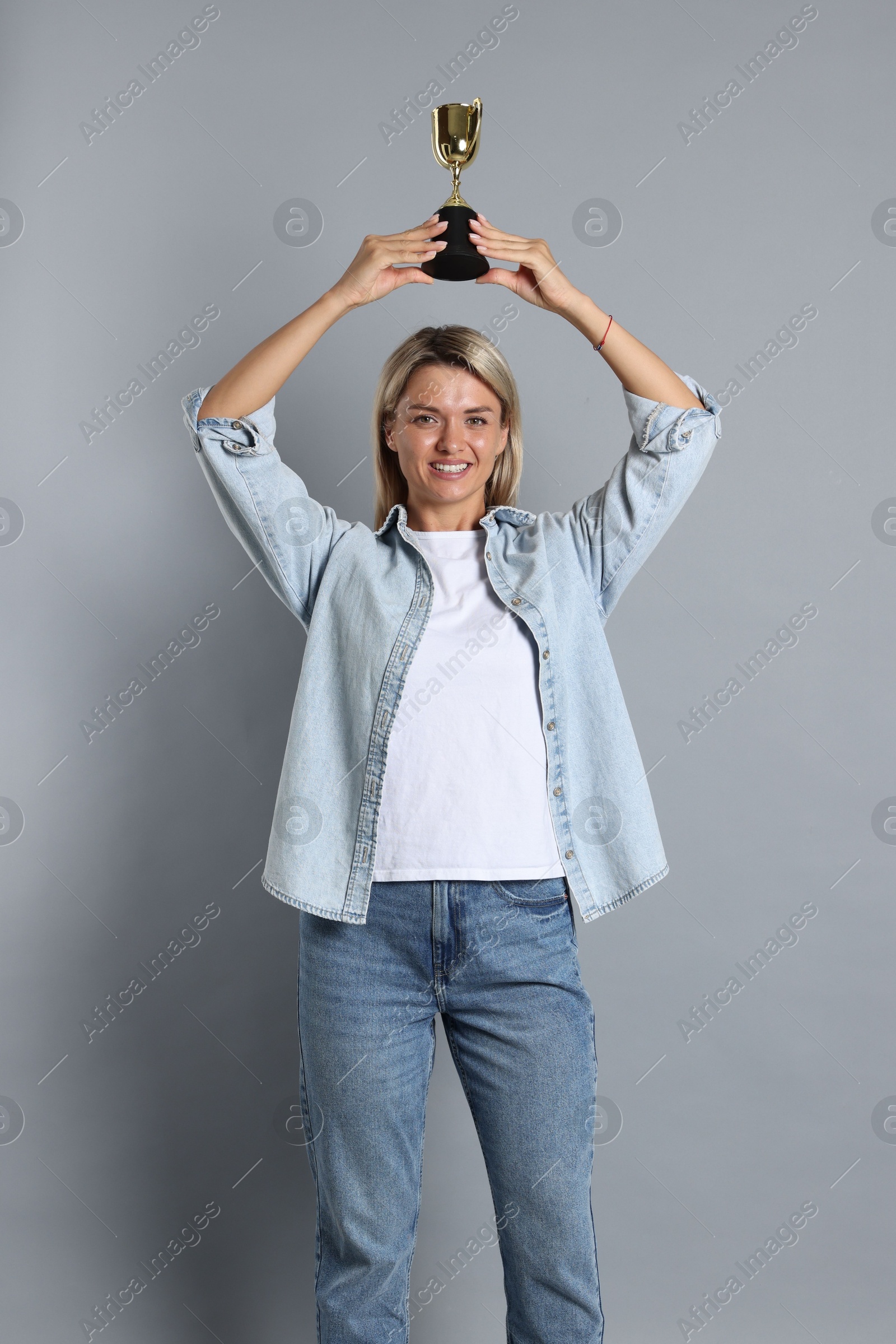 Photo of Happy winner with golden trophy cup on gray background