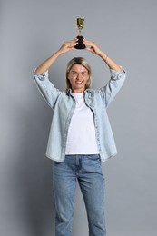 Photo of Happy winner with golden trophy cup on gray background