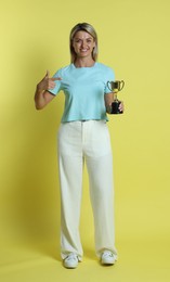 Photo of Happy winner with golden trophy cup on yellow background