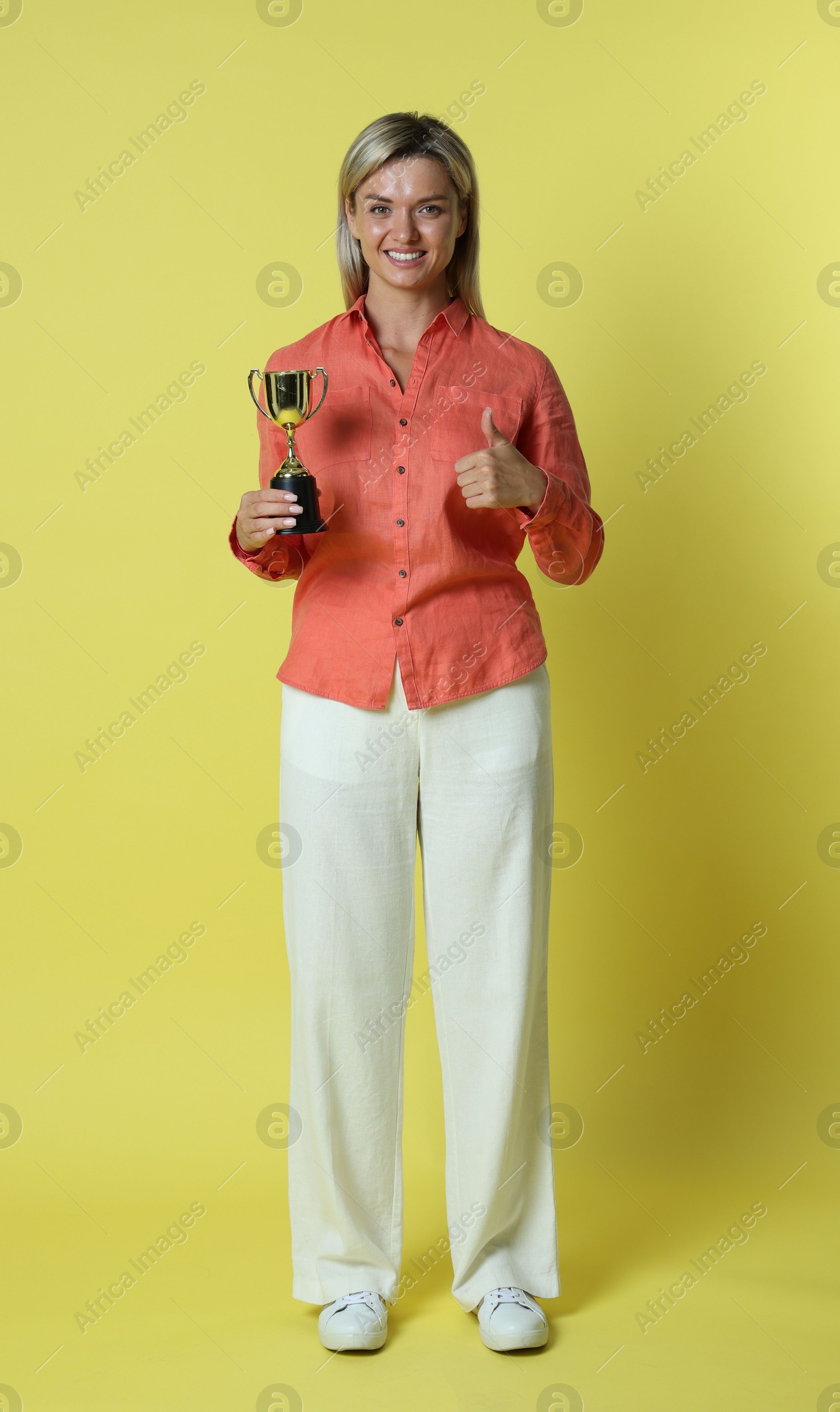 Photo of Happy winner with golden trophy cup showing thumbs up on yellow background