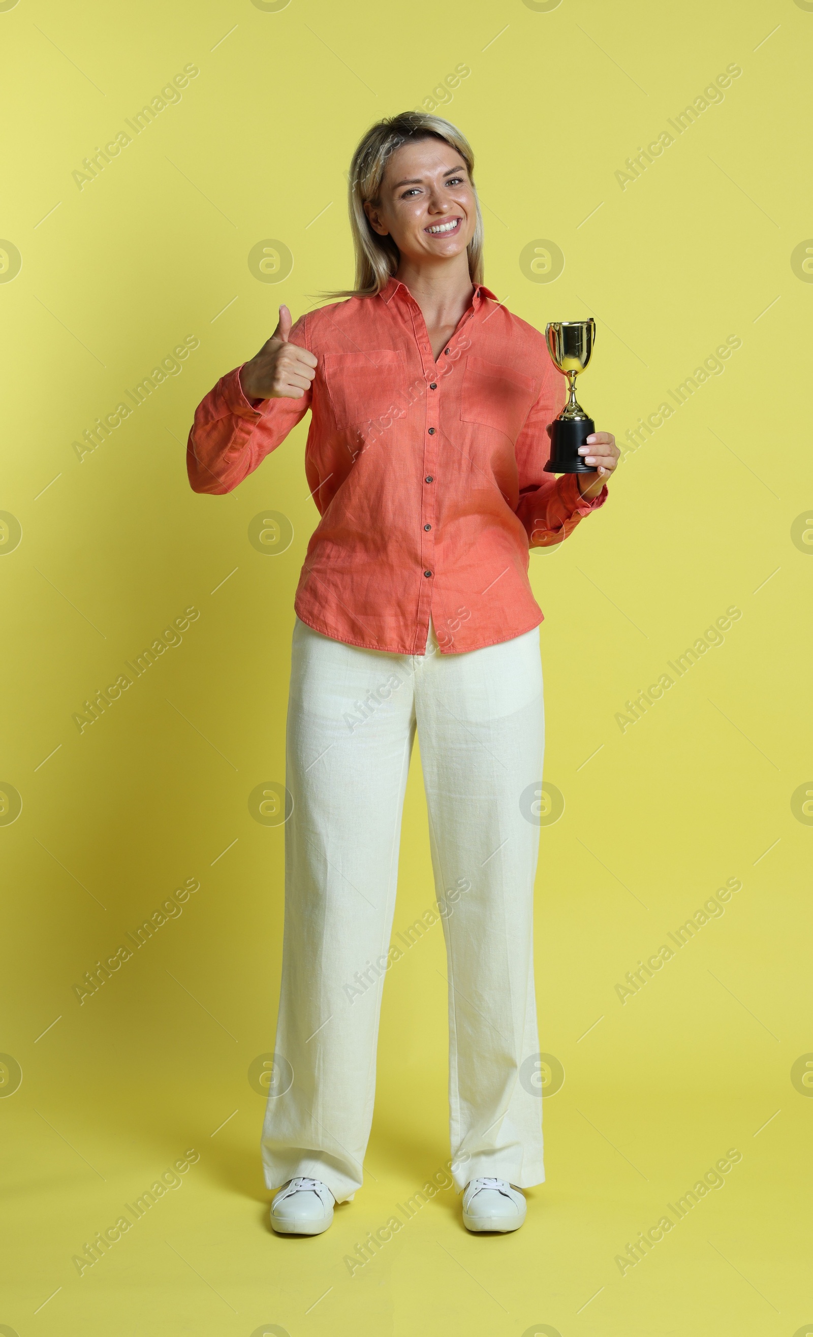 Photo of Happy winner with golden trophy cup showing thumbs up on yellow background