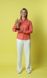 Photo of Happy winner with golden trophy cup on yellow background