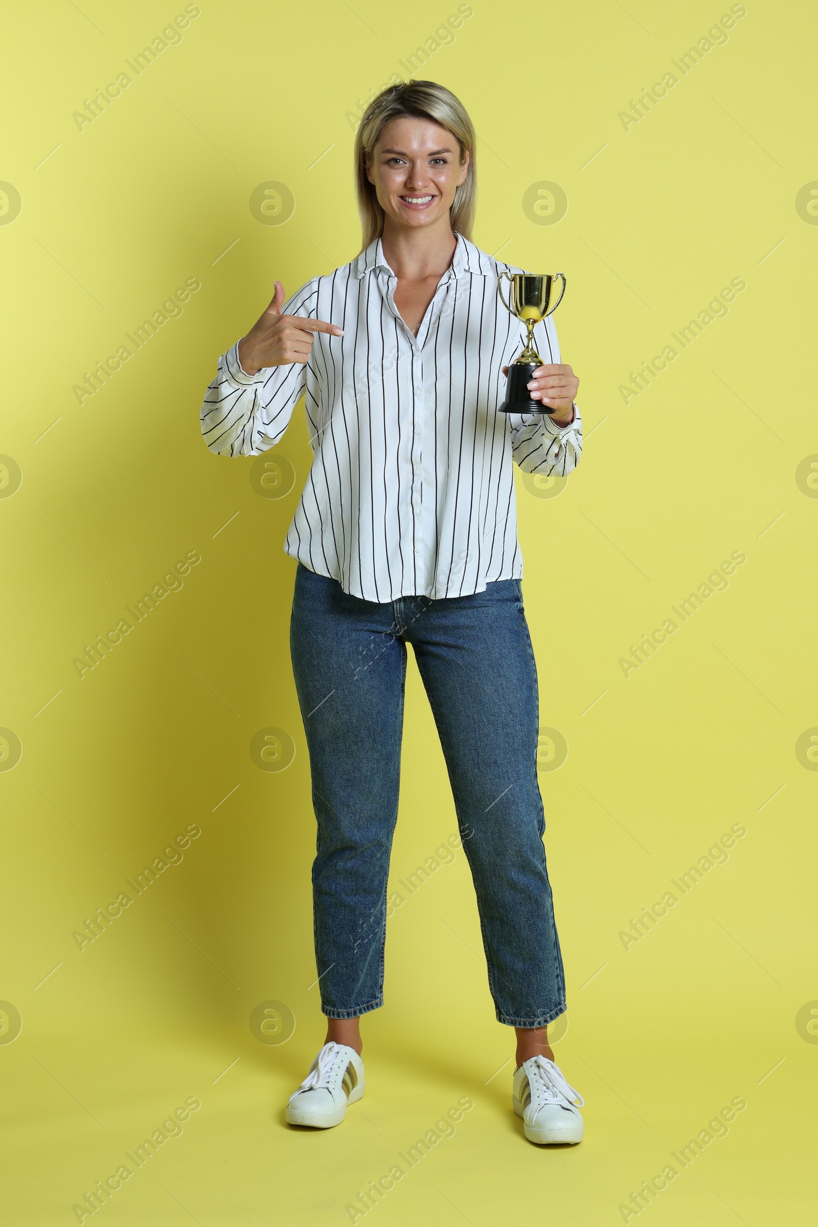 Photo of Happy winner with golden trophy cup on yellow background