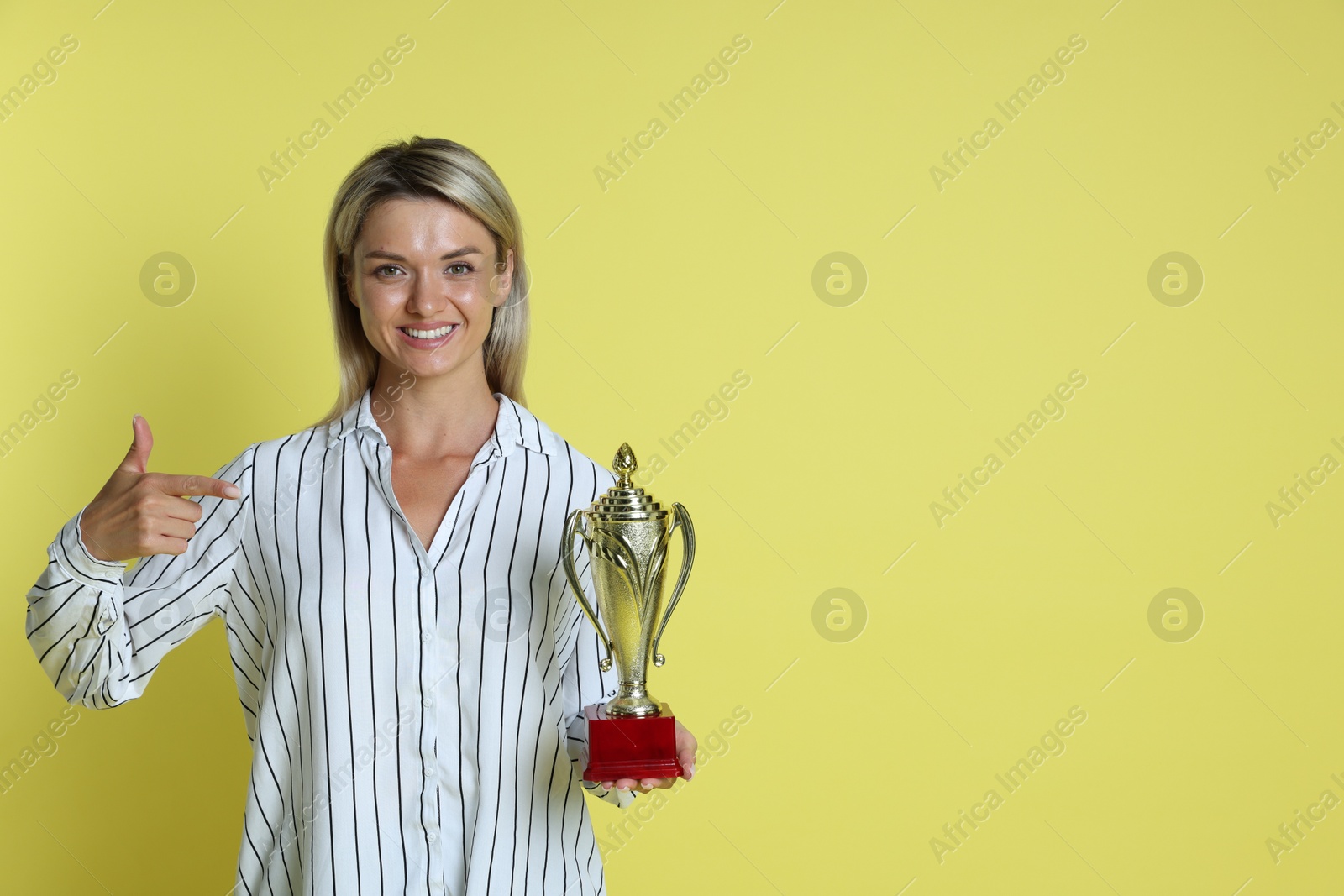 Photo of Happy winner with golden trophy cup on yellow background, space for text