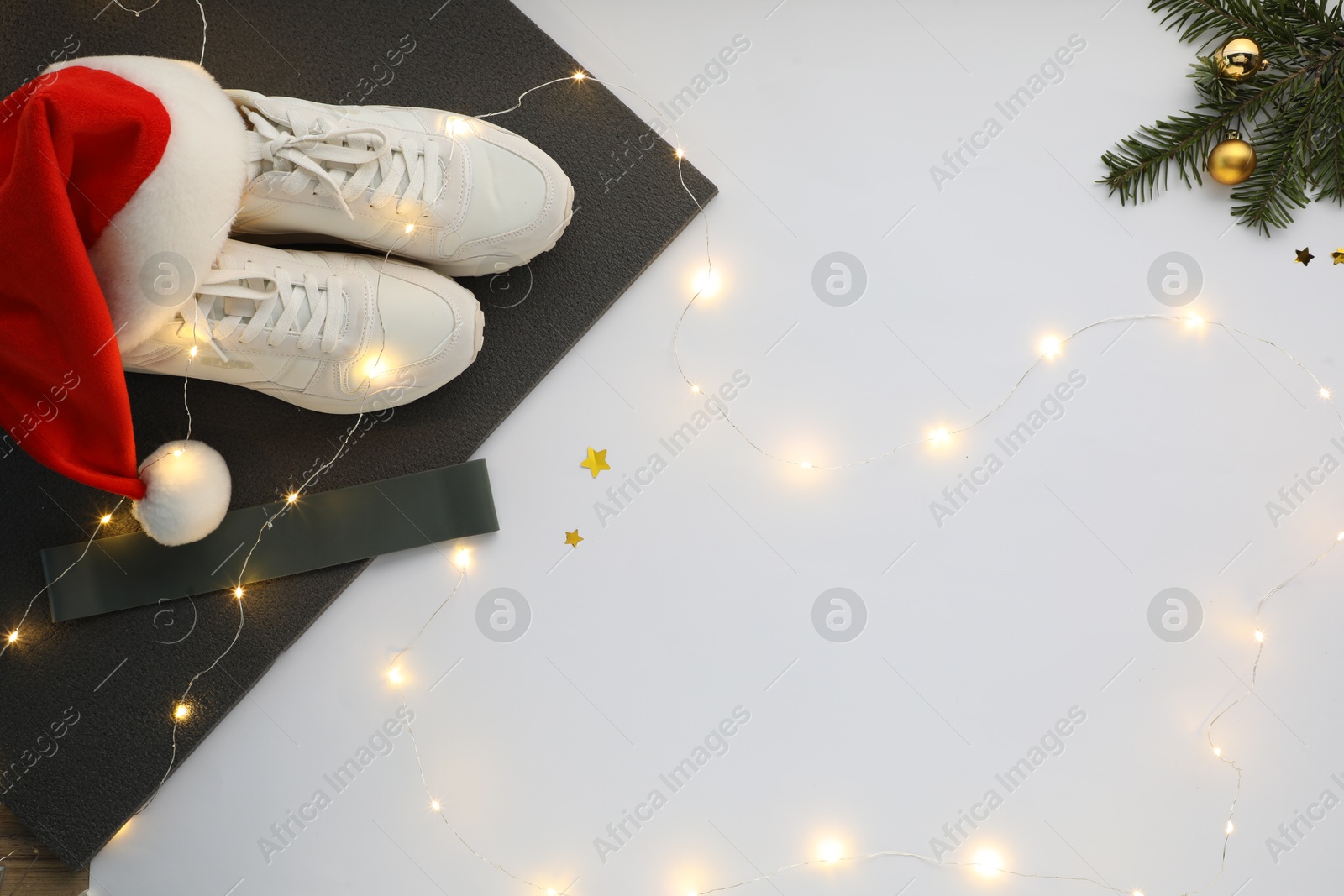 Photo of Yoga mat, sneakers, Santa hat, band and Christmas decor on white background, flat lay. Space for text