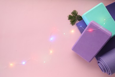 Photo of Yoga mat, blocks and Christmas decor on pink background, flat lay. Space for text