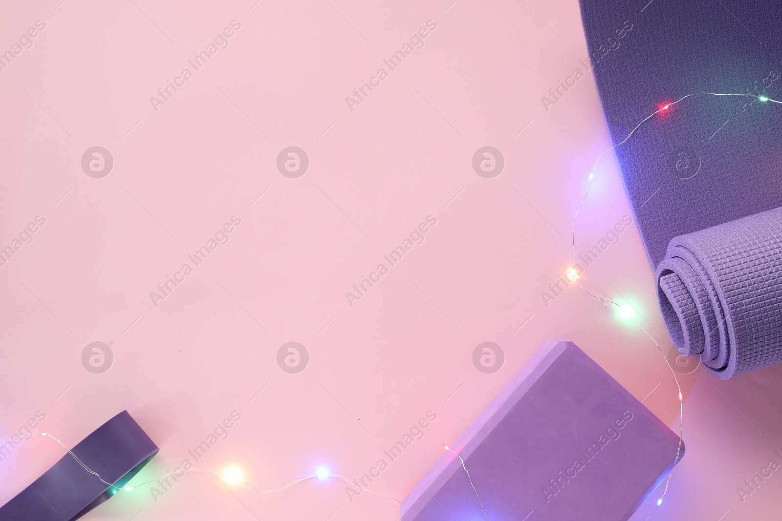 Photo of Yoga mat, fitness equipment and Christmas lights on pink background, flat lay. Space for text