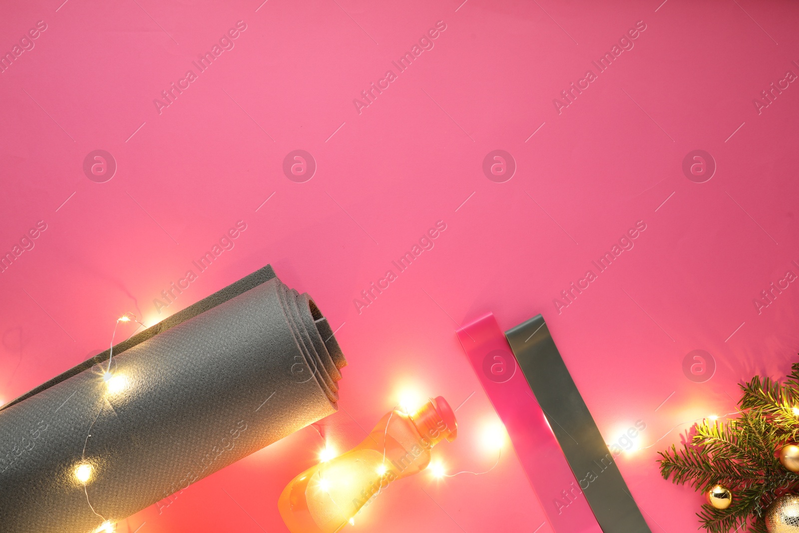 Photo of Yoga mat, bands, bottle and Christmas decor on pink background, flat lay. Space for text