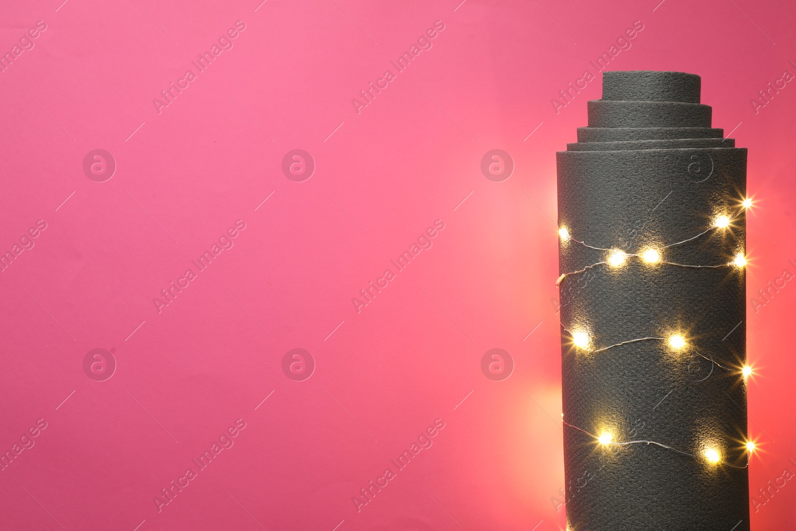 Photo of Yoga mat and Christmas lights on pink background, top view. Space for text