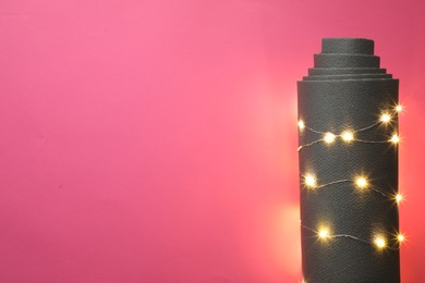 Photo of Yoga mat and Christmas lights on pink background, top view. Space for text