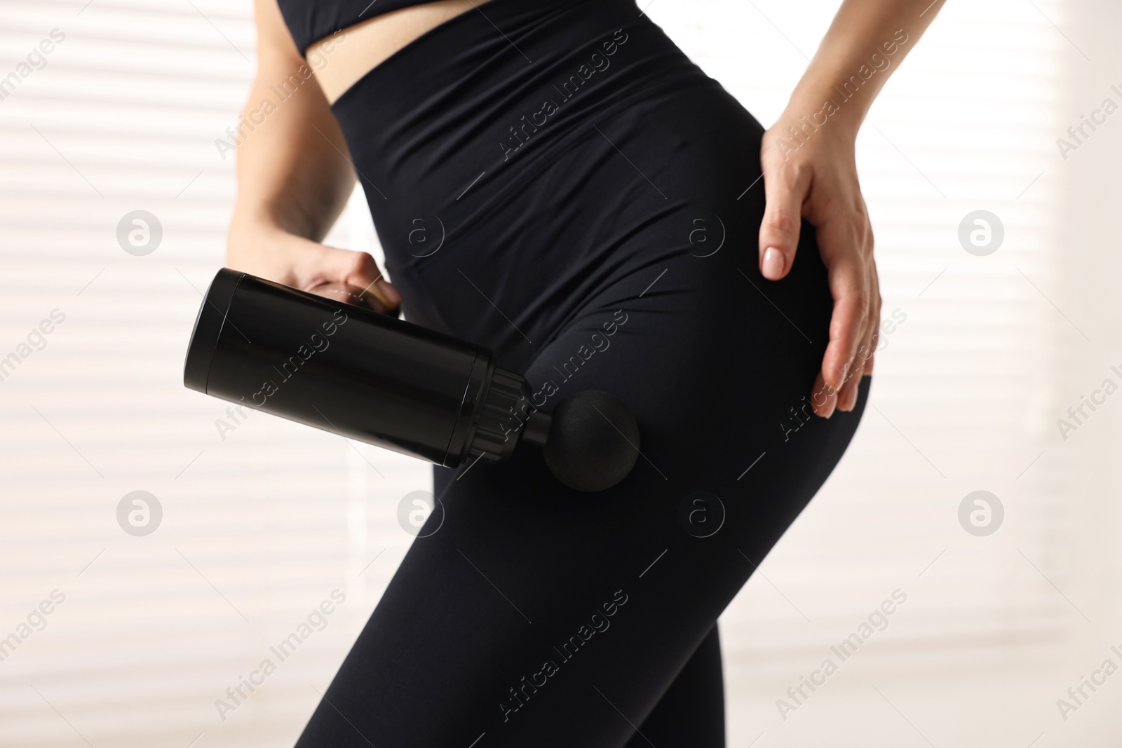 Photo of Woman using percussive massager to relax hip muscles indoors, closeup