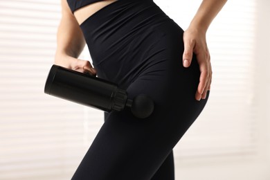 Photo of Woman using percussive massager to relax hip muscles indoors, closeup