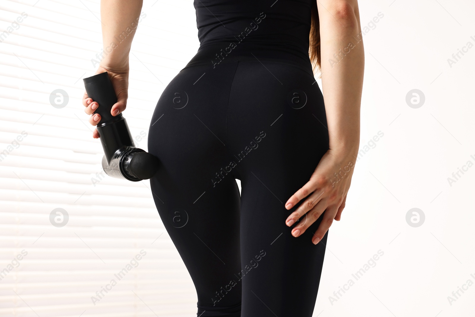 Photo of Woman using percussive massager to relax buttock muscles indoors, closeup