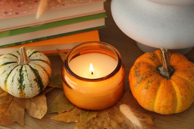 Photo of Burning candle, pumpkins and stack of books on wooden table, closeup. Autumn atmosphere