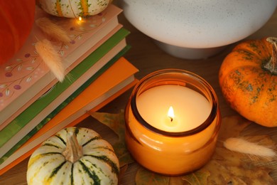 Photo of Burning candle, pumpkins and stack of books on wooden table, closeup. Autumn atmosphere