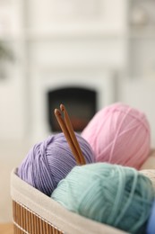 Many colorful yarns and crochet hooks in basket on blurred background, closeup. Space for text