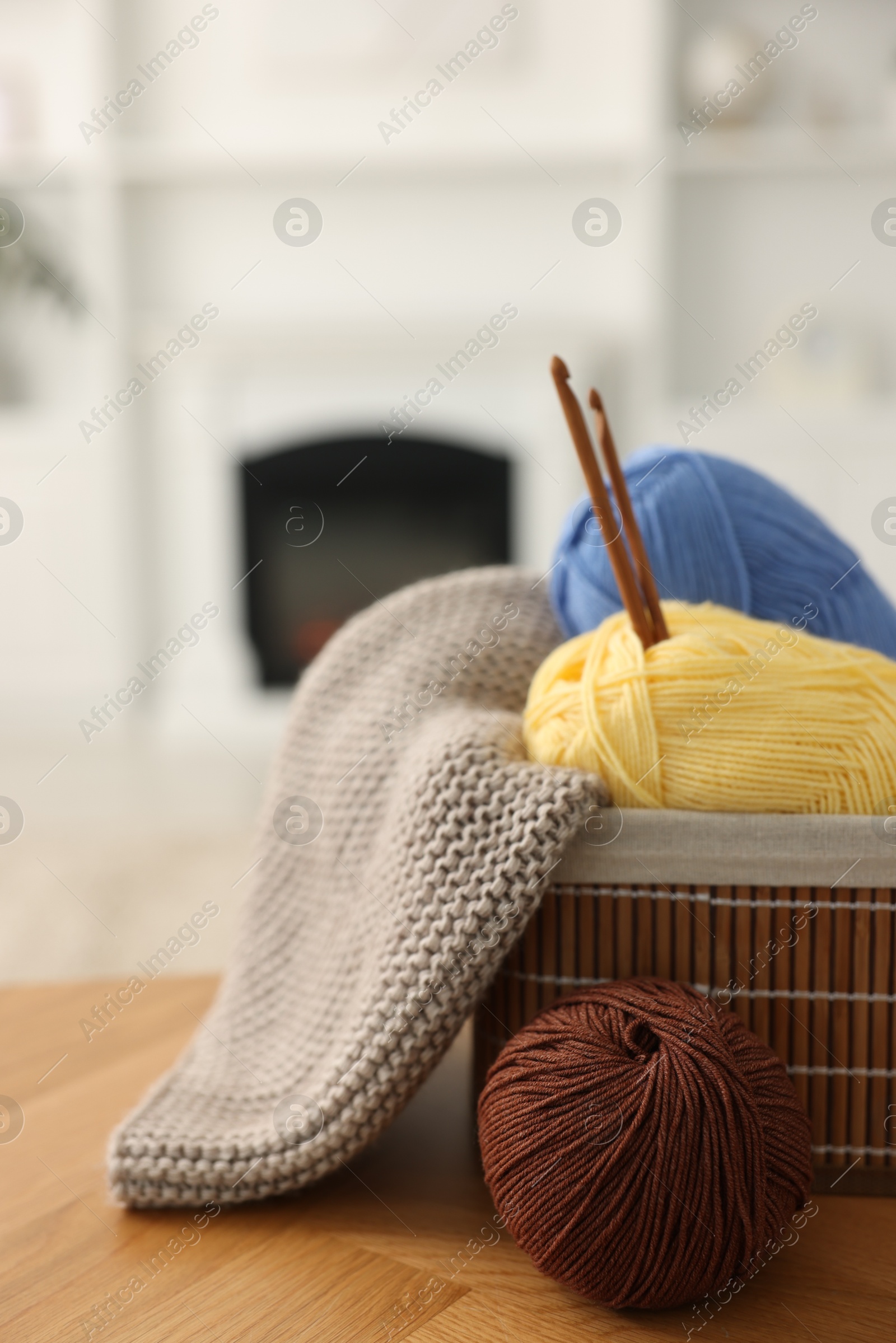 Photo of Colorful yarns, knitting sample, crochet hooks and basket on wooden table indoors, closeup. Space for text