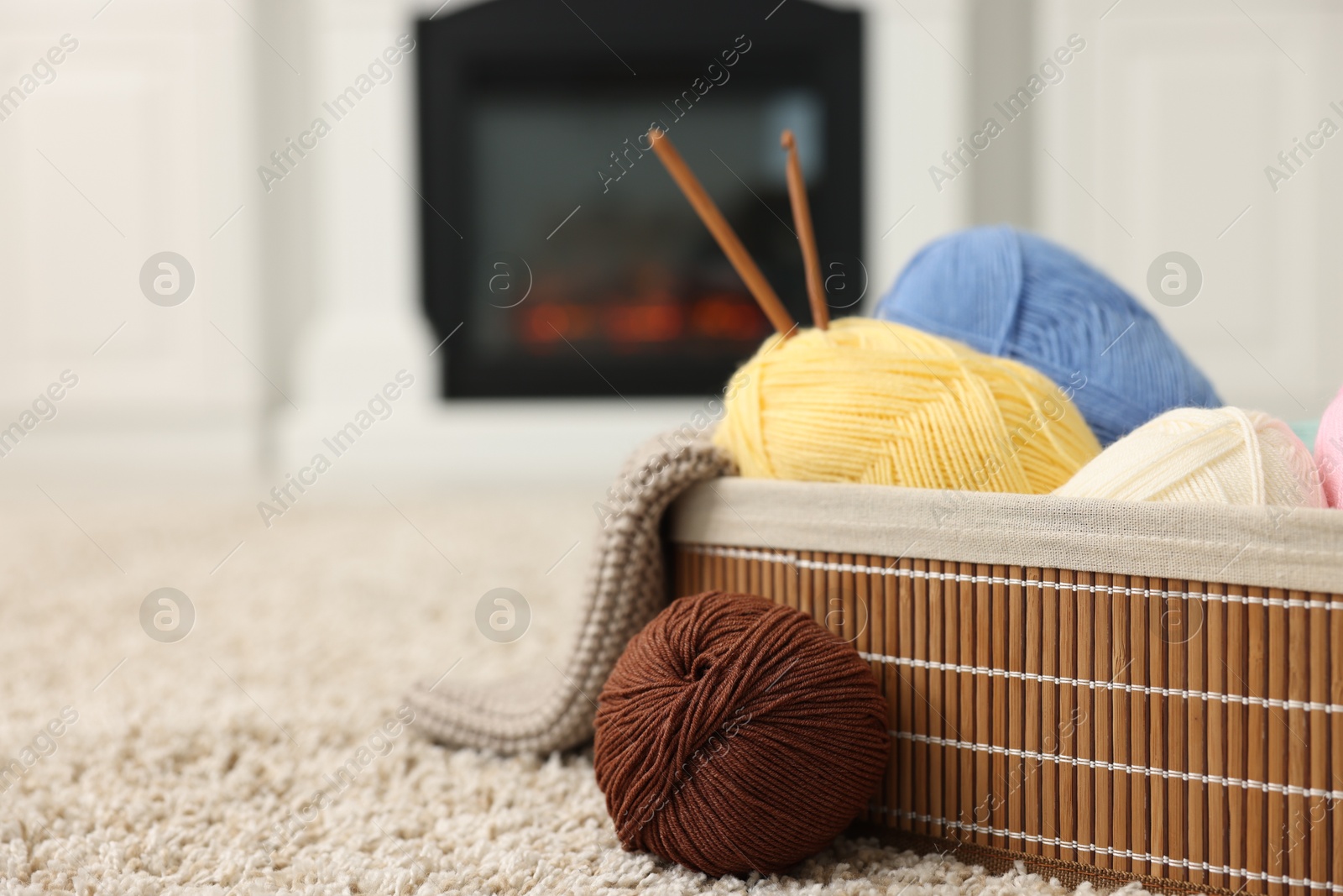 Photo of Colorful yarns, knitting sample, crochet hooks and basket on soft carpet indoors, closeup. Space for text