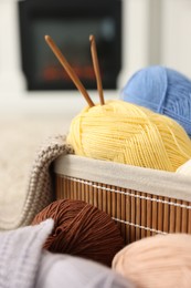 Colorful yarns, knitting sample, crochet hooks and basket indoors, closeup