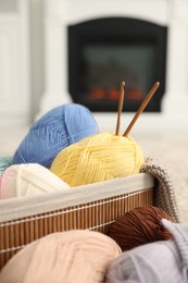 Photo of Colorful yarns, knitting sample, crochet hooks and basket indoors, closeup